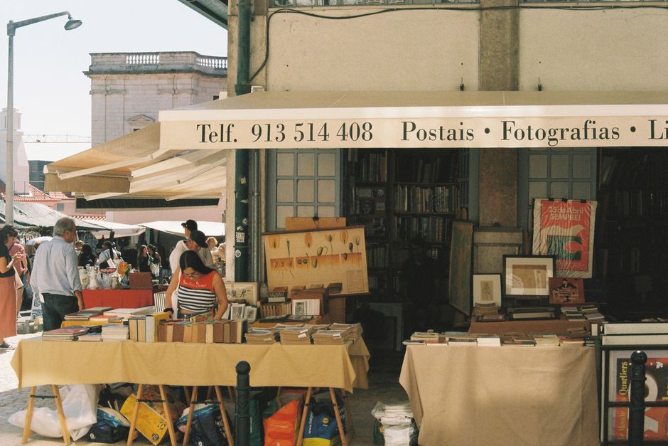 Colorful street market in Lisbon with a book stand displaying items on a sunny day.