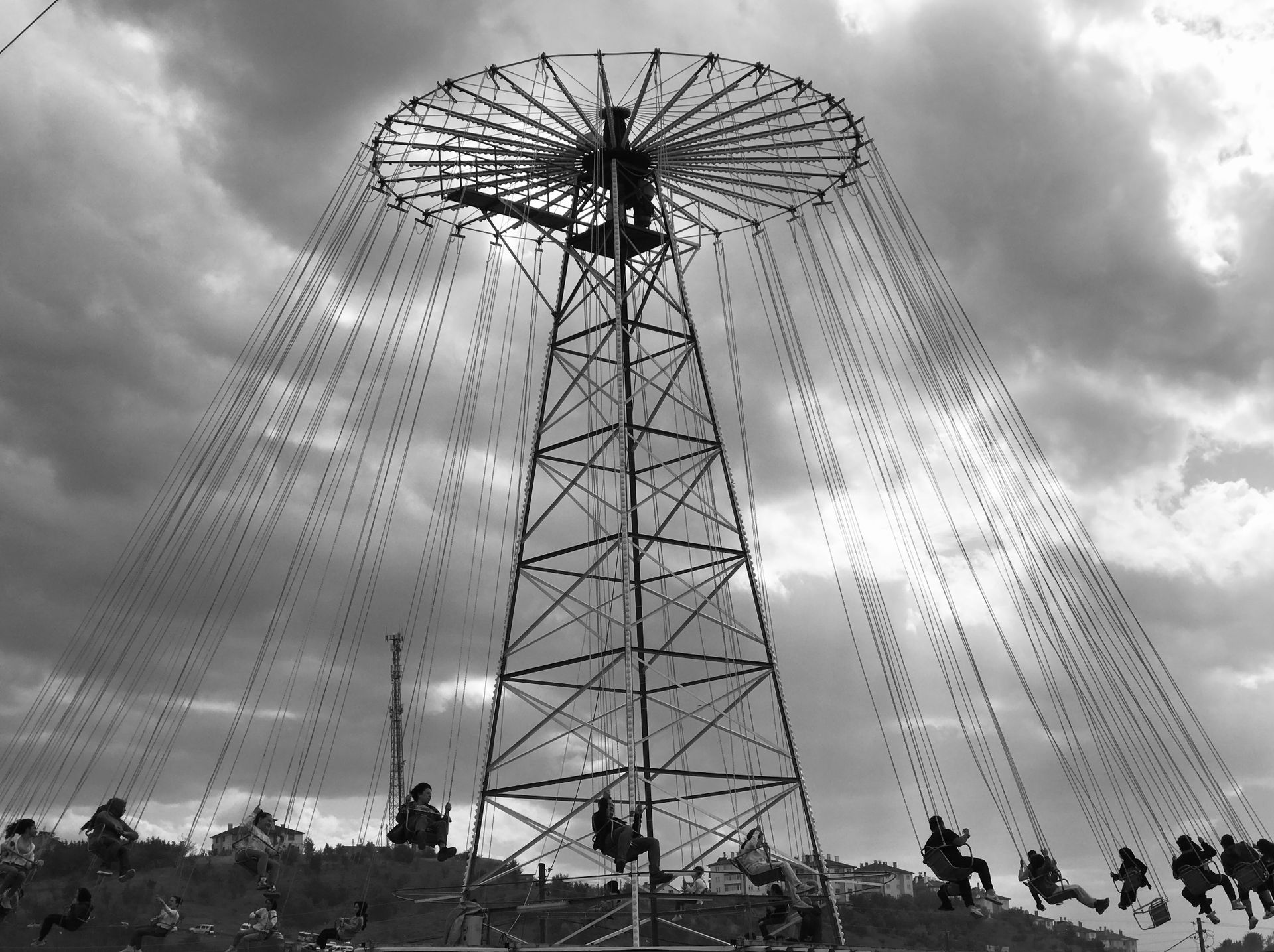 People enjoy a thrilling chair swing ride at an amusement park under cloudy skies.