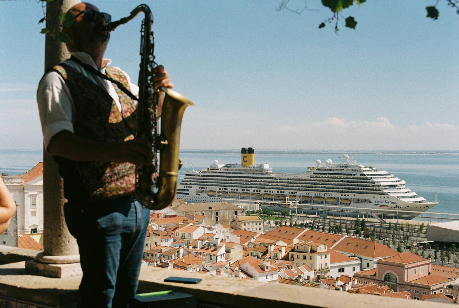 A saxophonist plays with a scenic view of Lisbon and a cruise ship in the background.