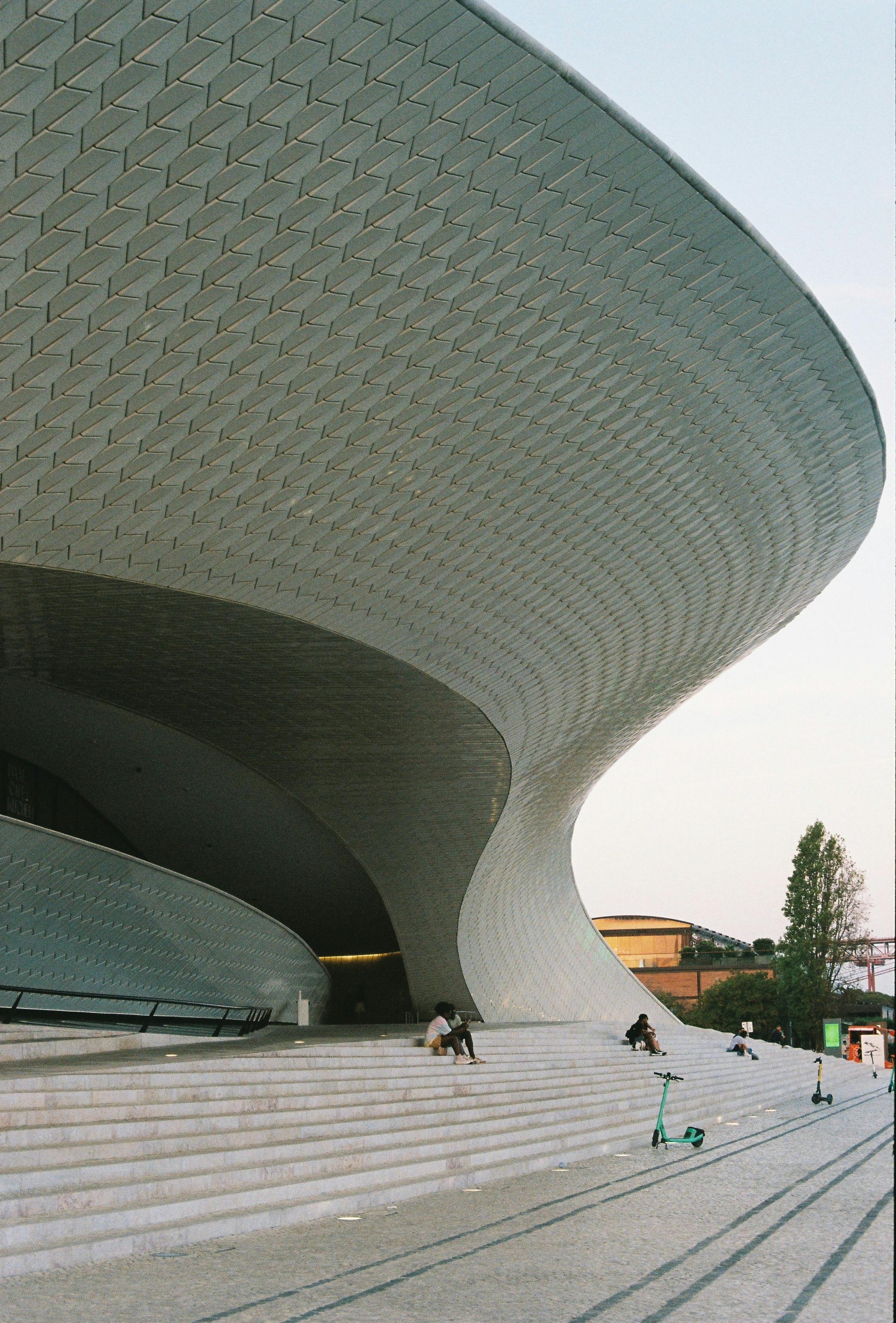 Modern architectural structure with people sitting and relaxing on the stairs beneath its futuristic curves.
