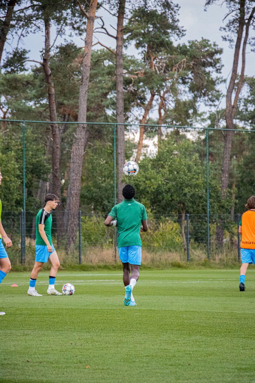 Atleten die voetbalskills oefenen op een bebost veld in België.