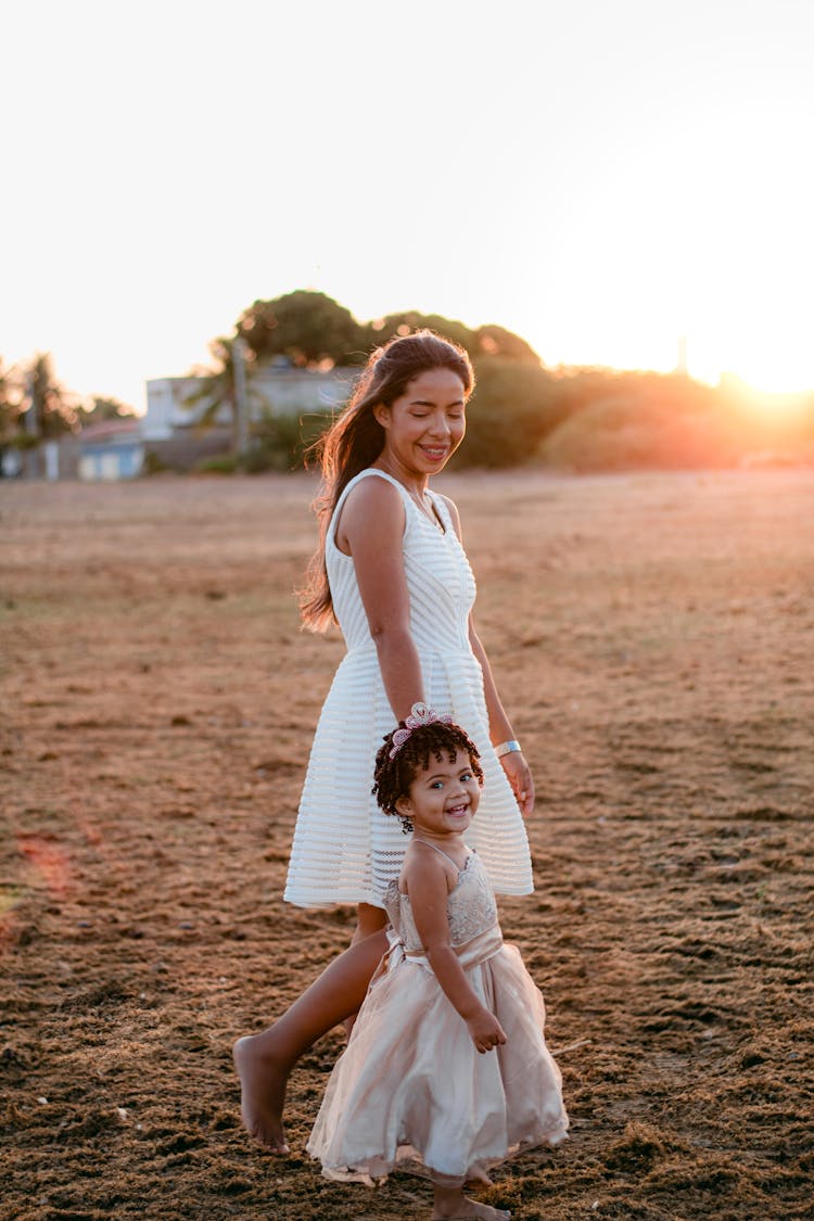 Woman And A Girl Wearing Bright Dresses Walking On Brown Soil