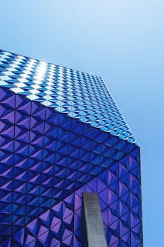 低角度视角下的现代建筑，其几何玻璃板反射着蓝天