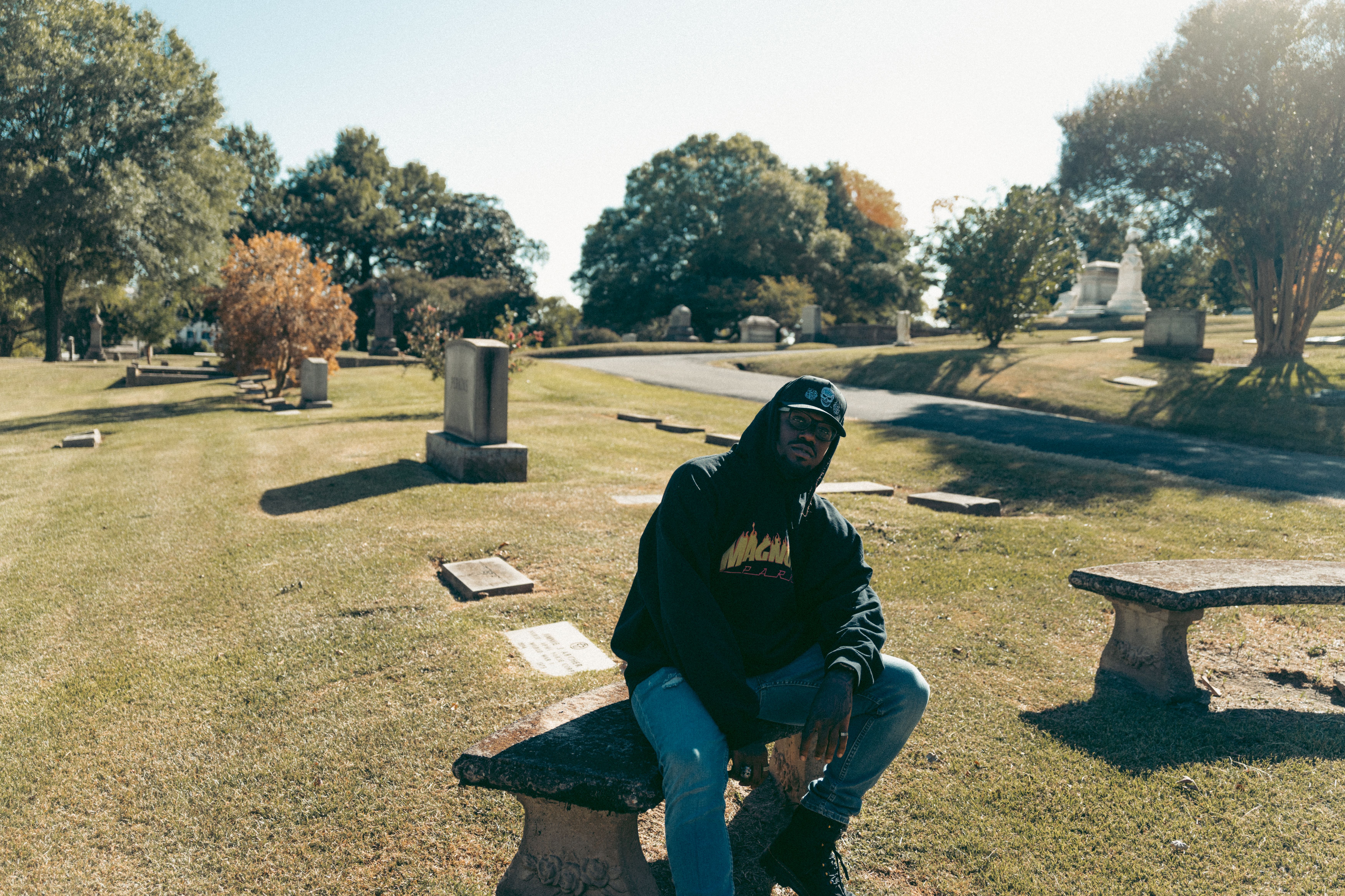 Man sitting in a serene cemetery, reflecting amid gravestones and autumn foliage.