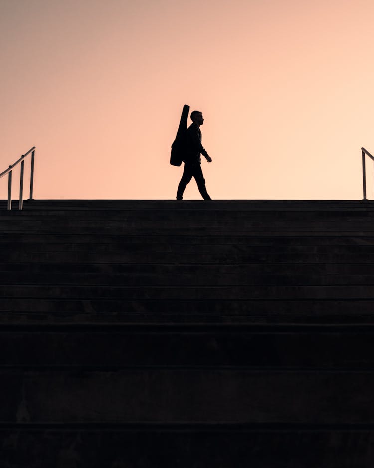 Silhouette Of A Person Carrying A Guitar