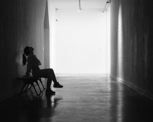 Free Black and white silhouette of a woman sitting thoughtfully on a bench in a minimalist hallway. Stock Photo