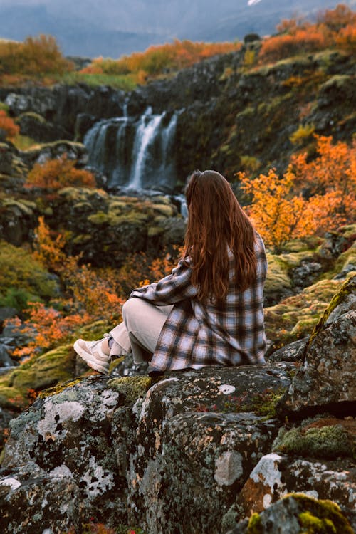 Woman Sitting on a Hill Looking at a Waterfall in Autumn 