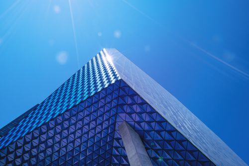 Free Modern architectural design featuring a tall glass building with geometric patterns against a clear blue sky. Stock Photo