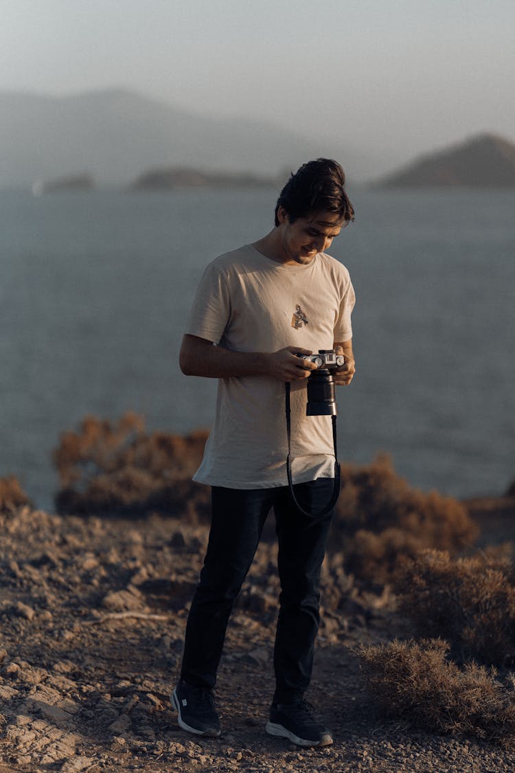 Man Standing On A Shore Holding A Camera And Smiling