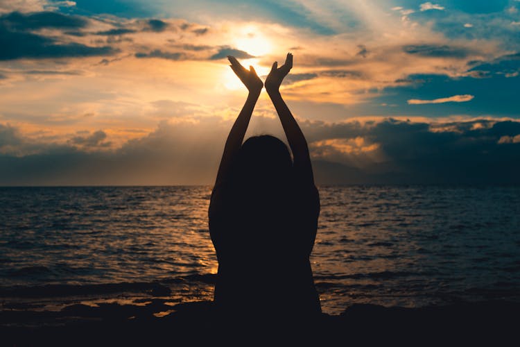 Person Raising Hands Near Sea At Sunset