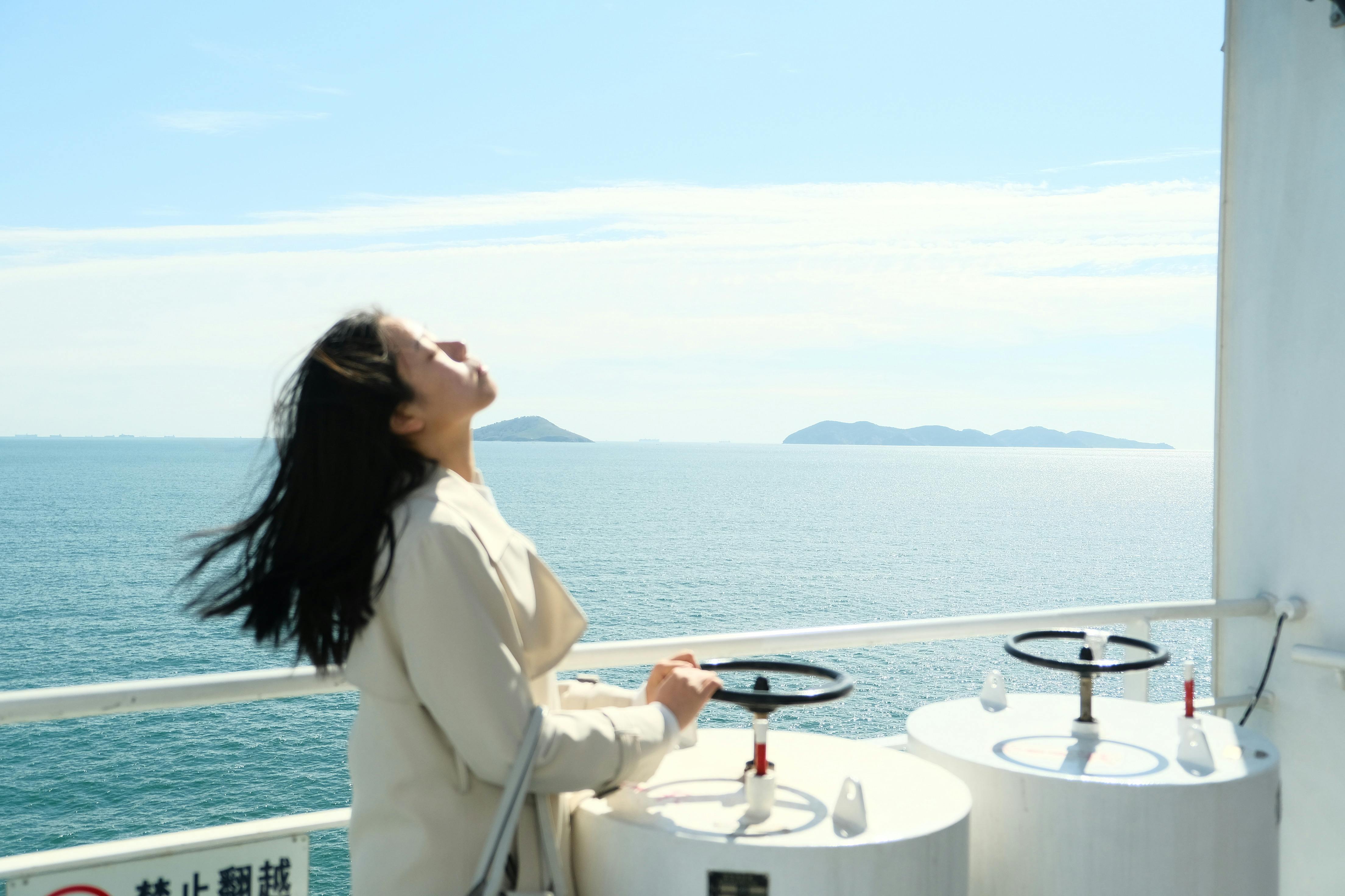 A woman stands on a boat, enjoying the sea breeze with a serene view in Dalian, China.