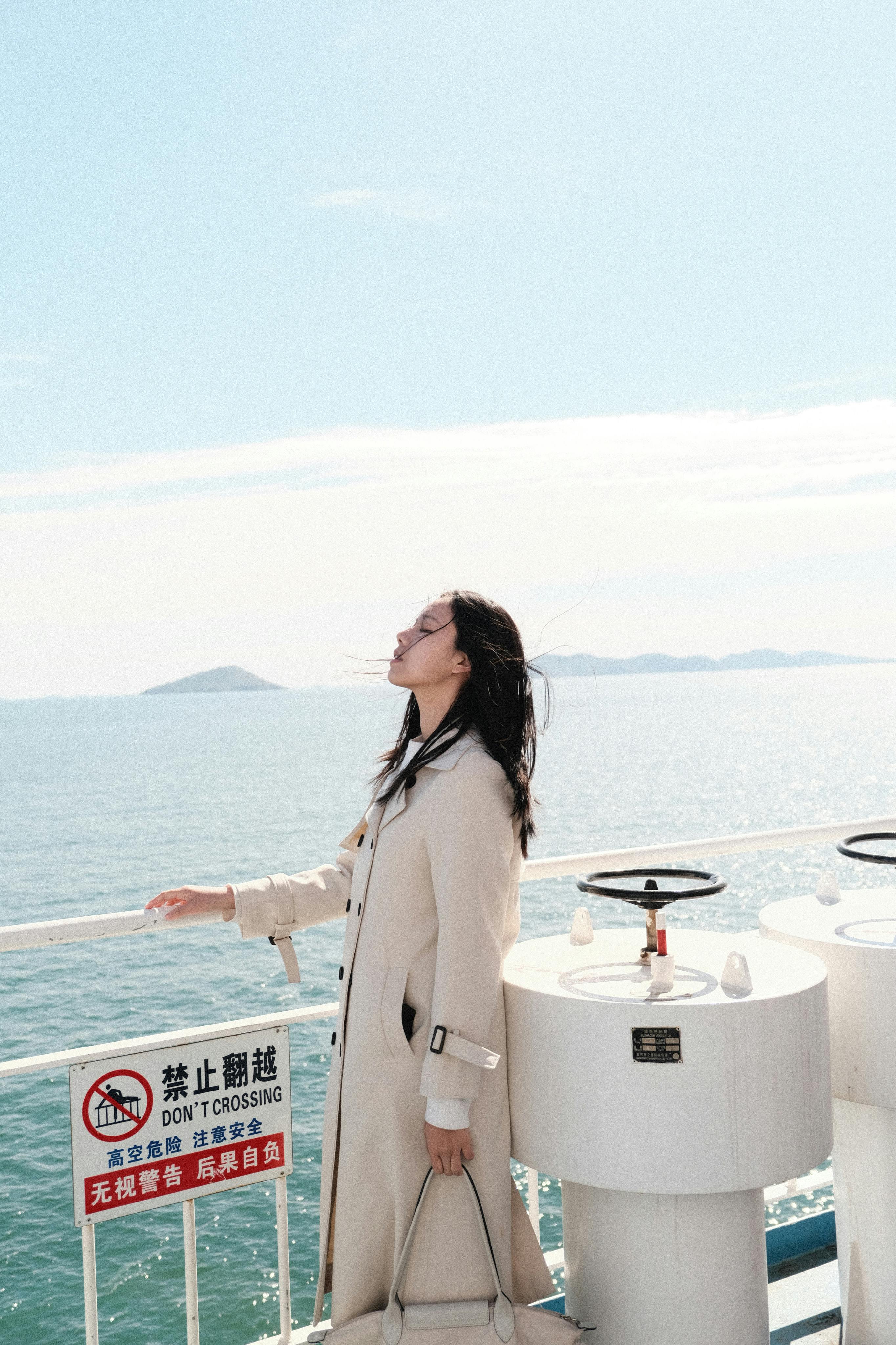 Woman in coat on a ferry deck, enjoying the sea breeze under a clear sky.