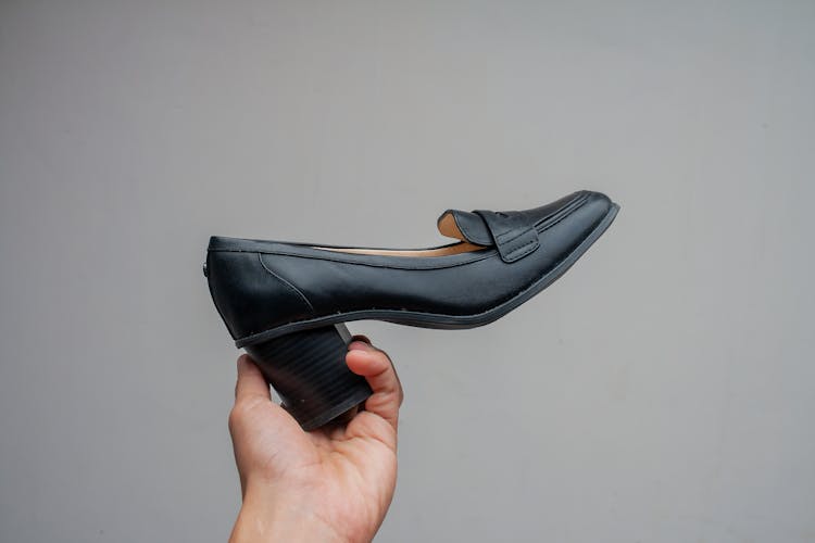 A Person Holding A Black Leather Shoe