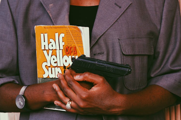 A Person's Hands Holding A Book And A Black Pistol