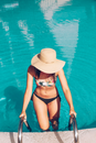 Woman Stepping Onto Pool Ladder Wearing Beige Sun Hat