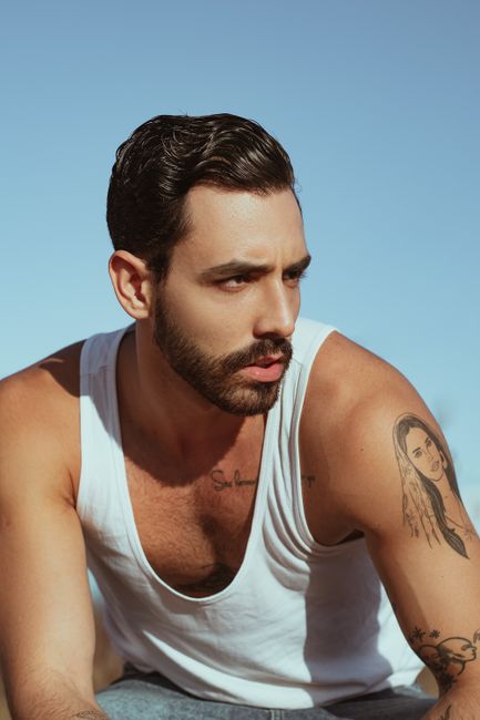 Sunlit portrait of a man in a tank top with tattoos, exuding modern style.