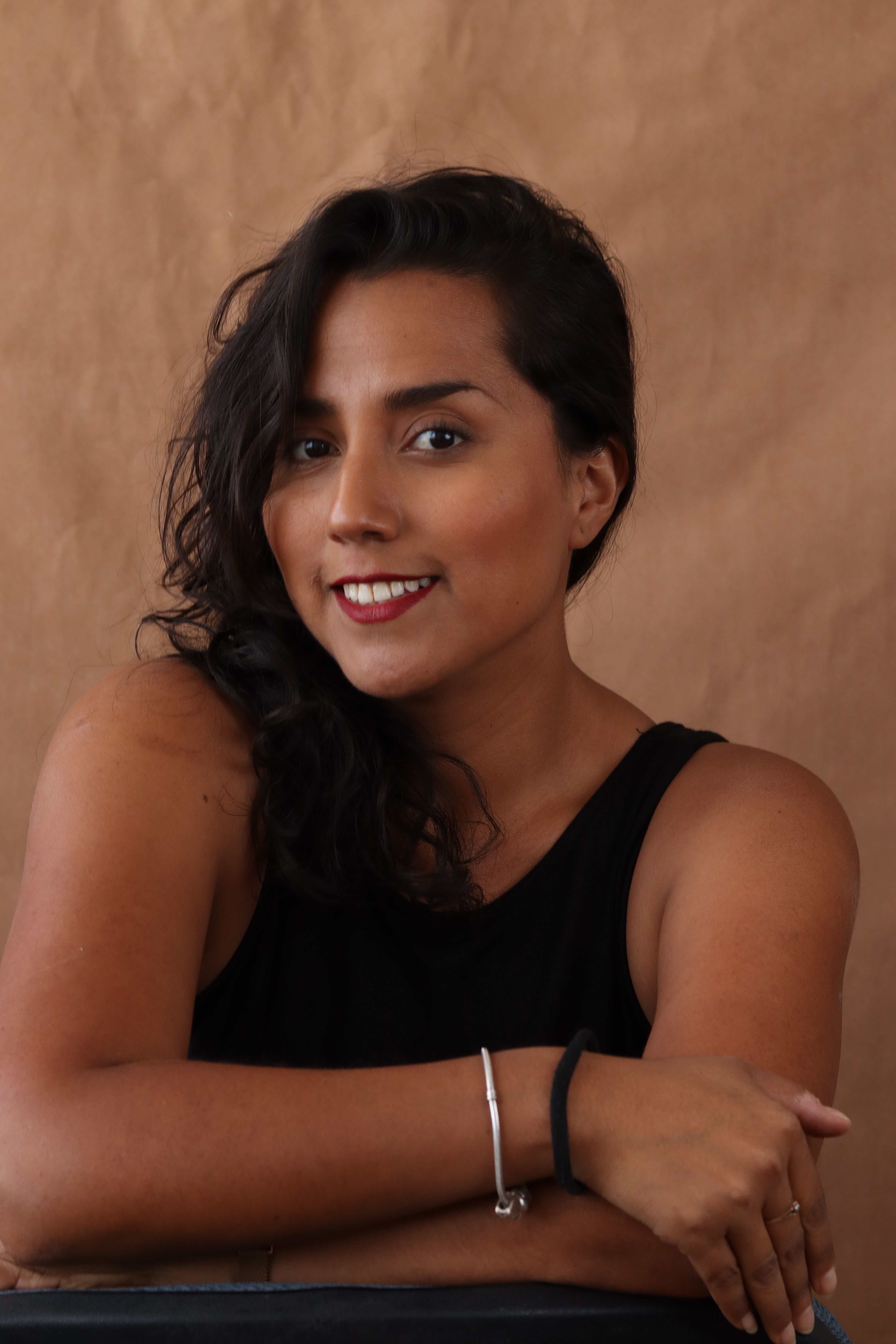 A smiling woman posing confidently in a studio with a neutral background.