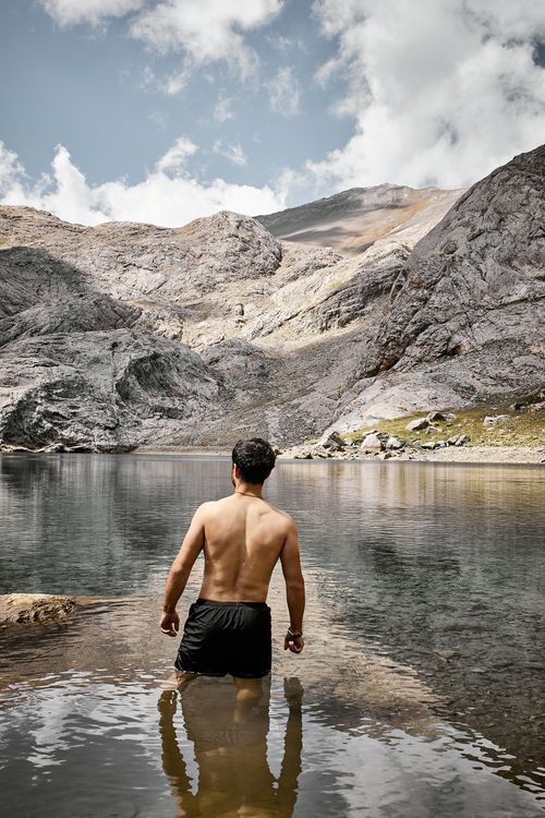 Free A man stands knee-deep in a clear mountain lake, surrounded by rocky landscapes and blue skies. Stock Photo