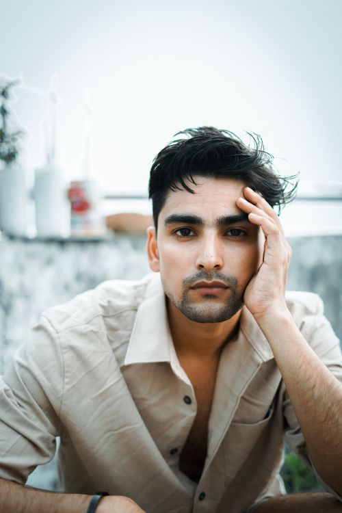 Free A thoughtful young man in casual wear poses outdoors, hand on face, looking directly at the camera. Stock Photo