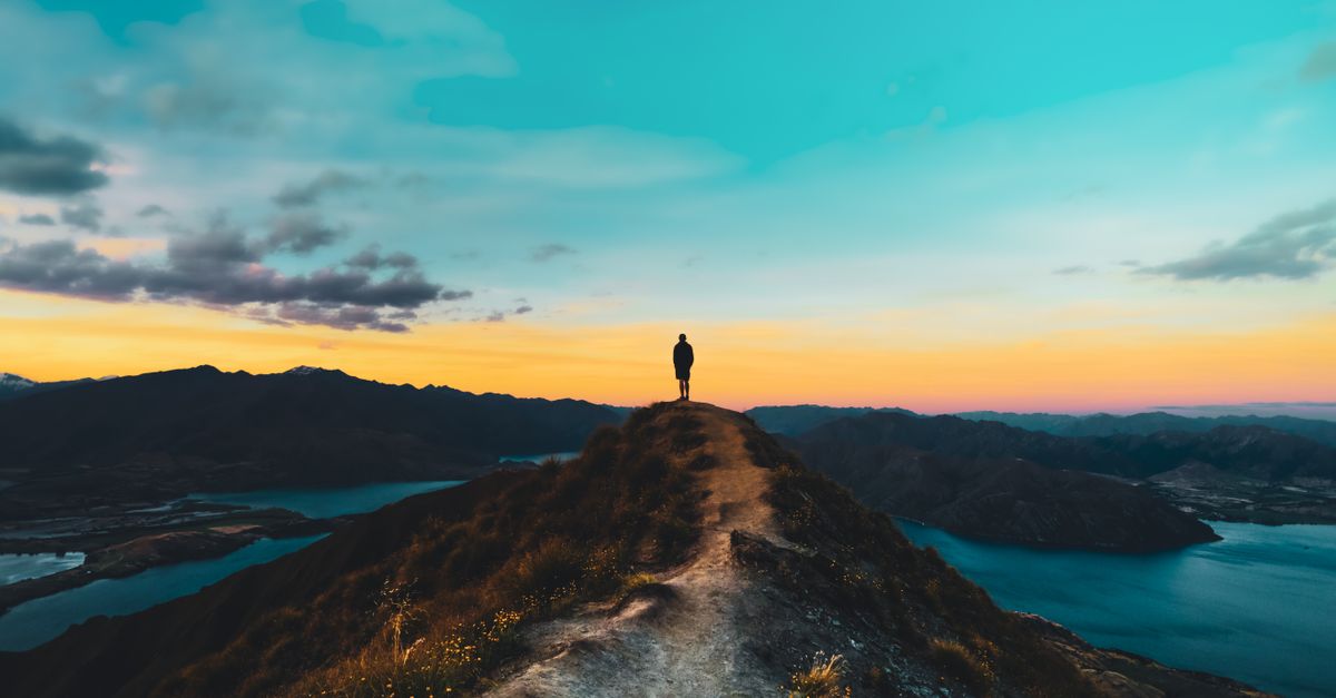 Person silhouetted on Roys Peak with breathtaking sunset view, Wanaka, New Zealand.