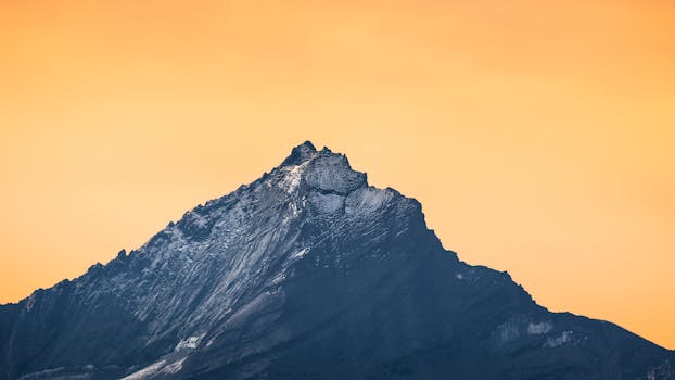 Scenic view of a rocky mountain peak against a vivid orange sky during sunset.