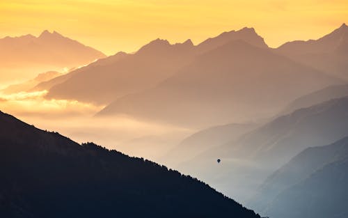 Hot Air Balloon Flight Over a Valley Among High Mountains at Sunset