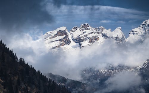 Fog Surrounding a Snow Covered Mountain Under Blue Sky