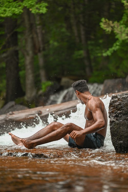 Man Sitting on the Base of a Waterfall