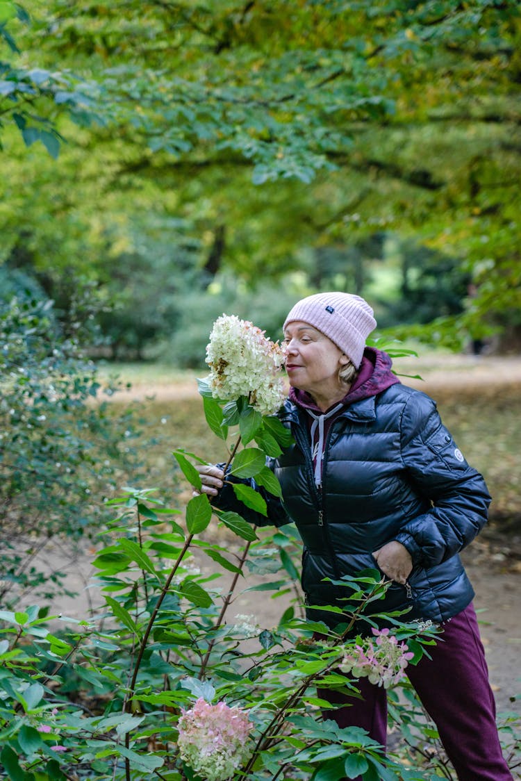 Woman In Blue Bubble Jacket Smelling A Cluster Of White Flower