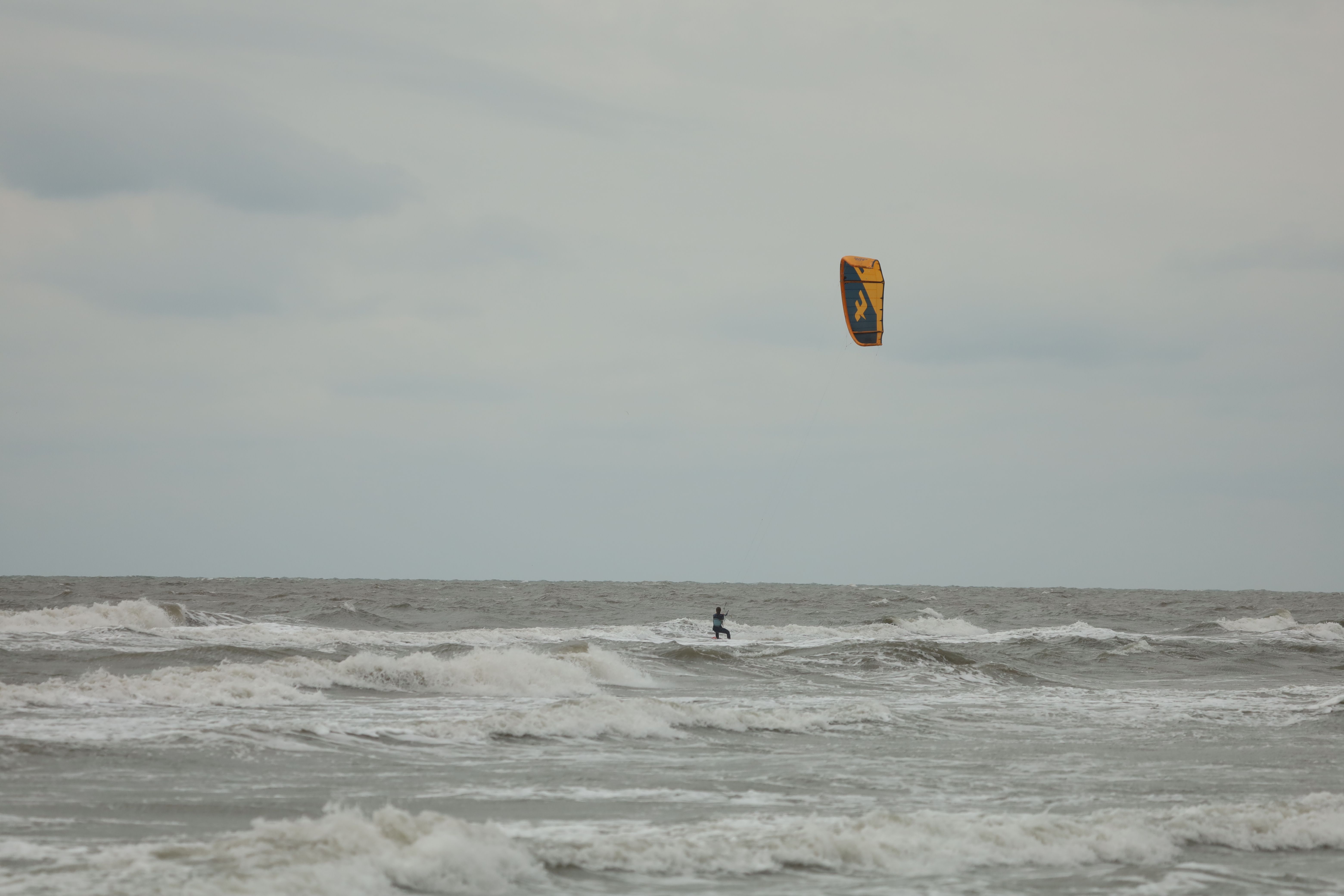 Kite surfer catching waves in the ocean under a cloudy sky, showcasing thrilling water sports.