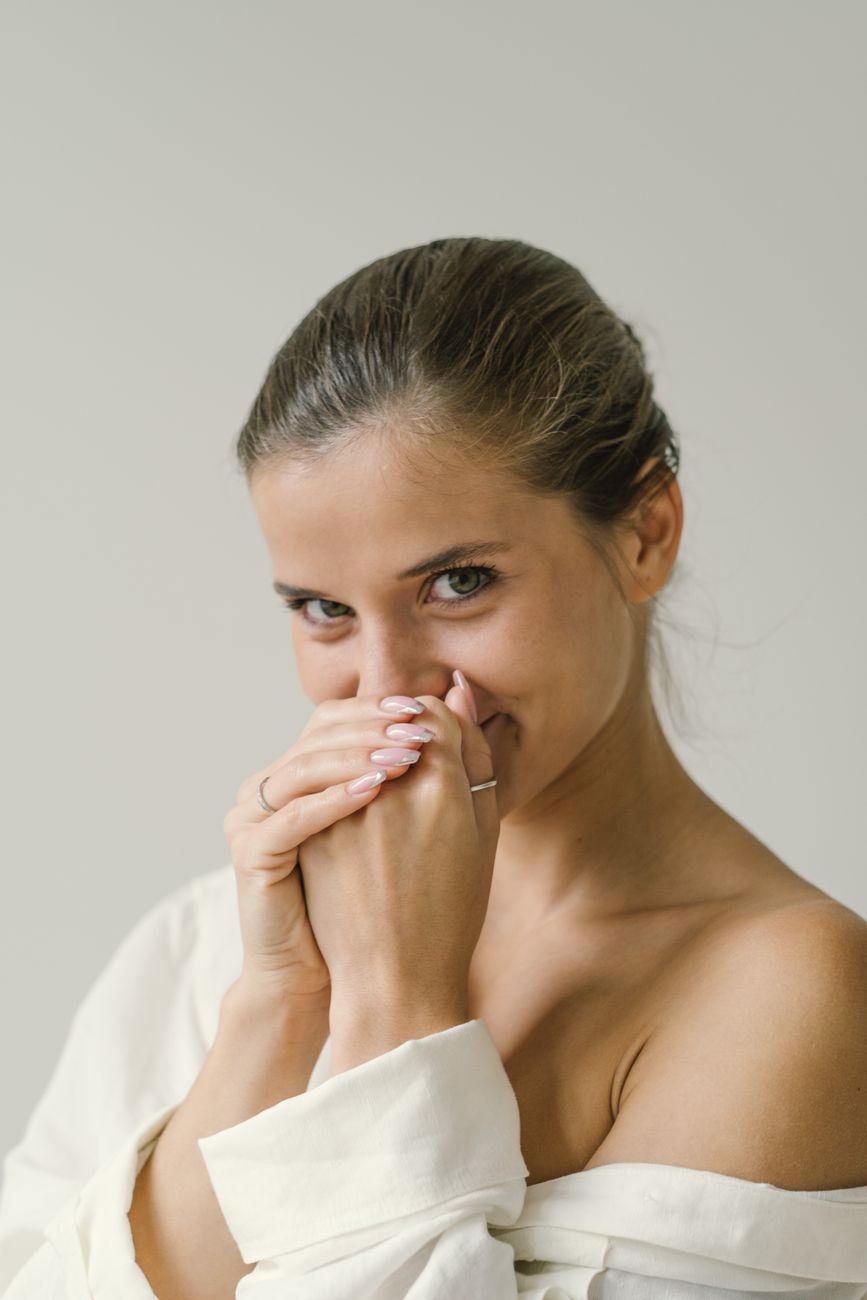 A close-up portrait of a young woman with hands near her face, exuding a playful and cheerful vibe.