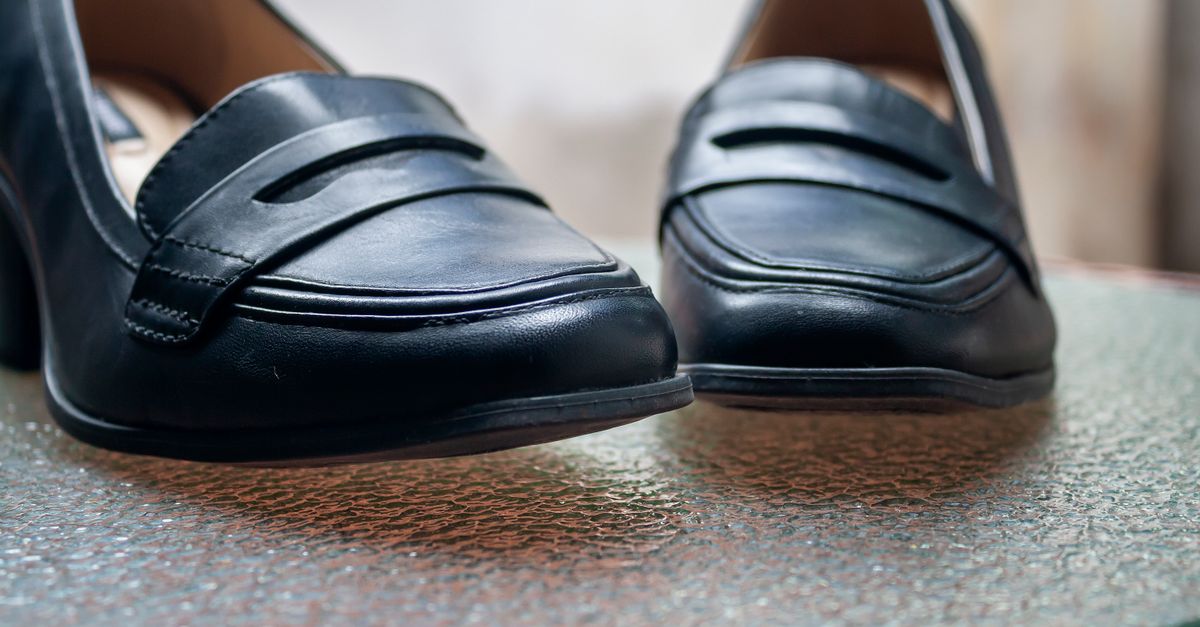 Close-up of stylish black leather women's shoes on a textured glass table.