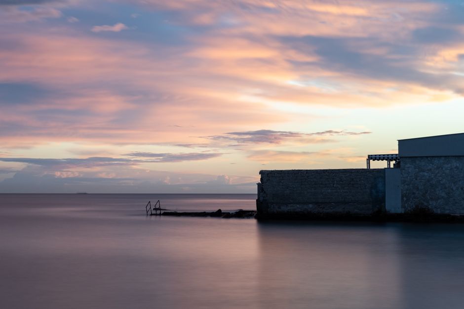Tranquil sunset over Bari harbor with vivid clouds reflecting on calm sea waters.