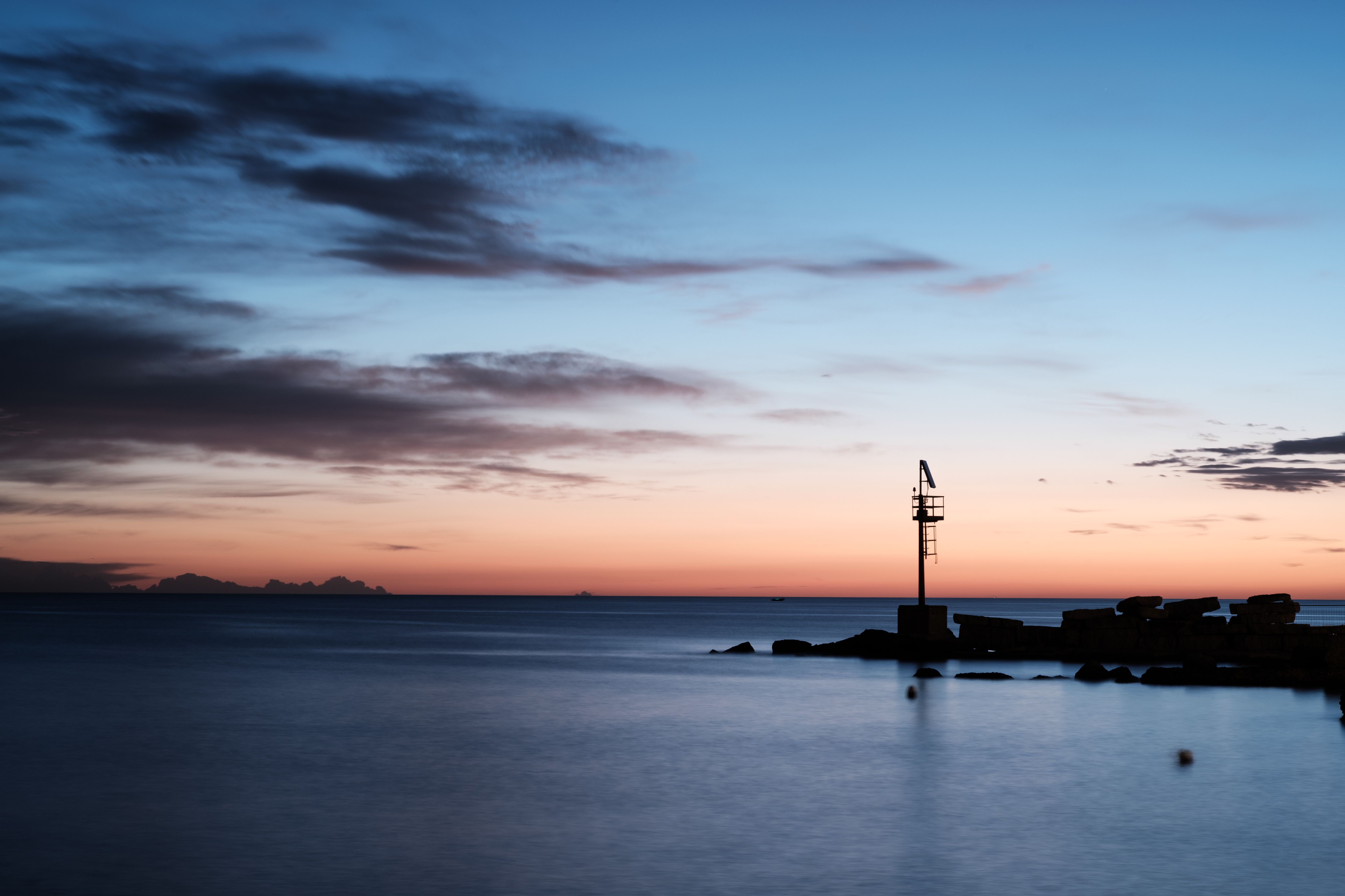Serene sunset by the sea with silhouetted pole in Bari, Italy. Calm waters under a vibrant sky.