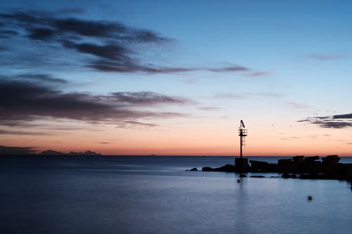 Free Serene sunset by the sea with silhouetted pole in Bari, Italy. Calm waters under a vibrant sky. Stock Photo