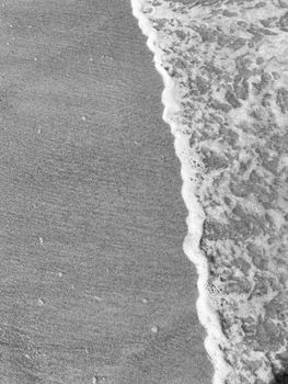 Close-up of gentle waves meeting the sandy beach in black and white.