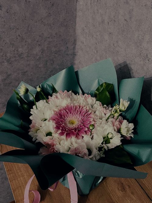 Free Charming bouquet of chrysanthemums wrapped in blue paper on a wooden table. Perfect for gifts and romantic occasions. Stock Photo