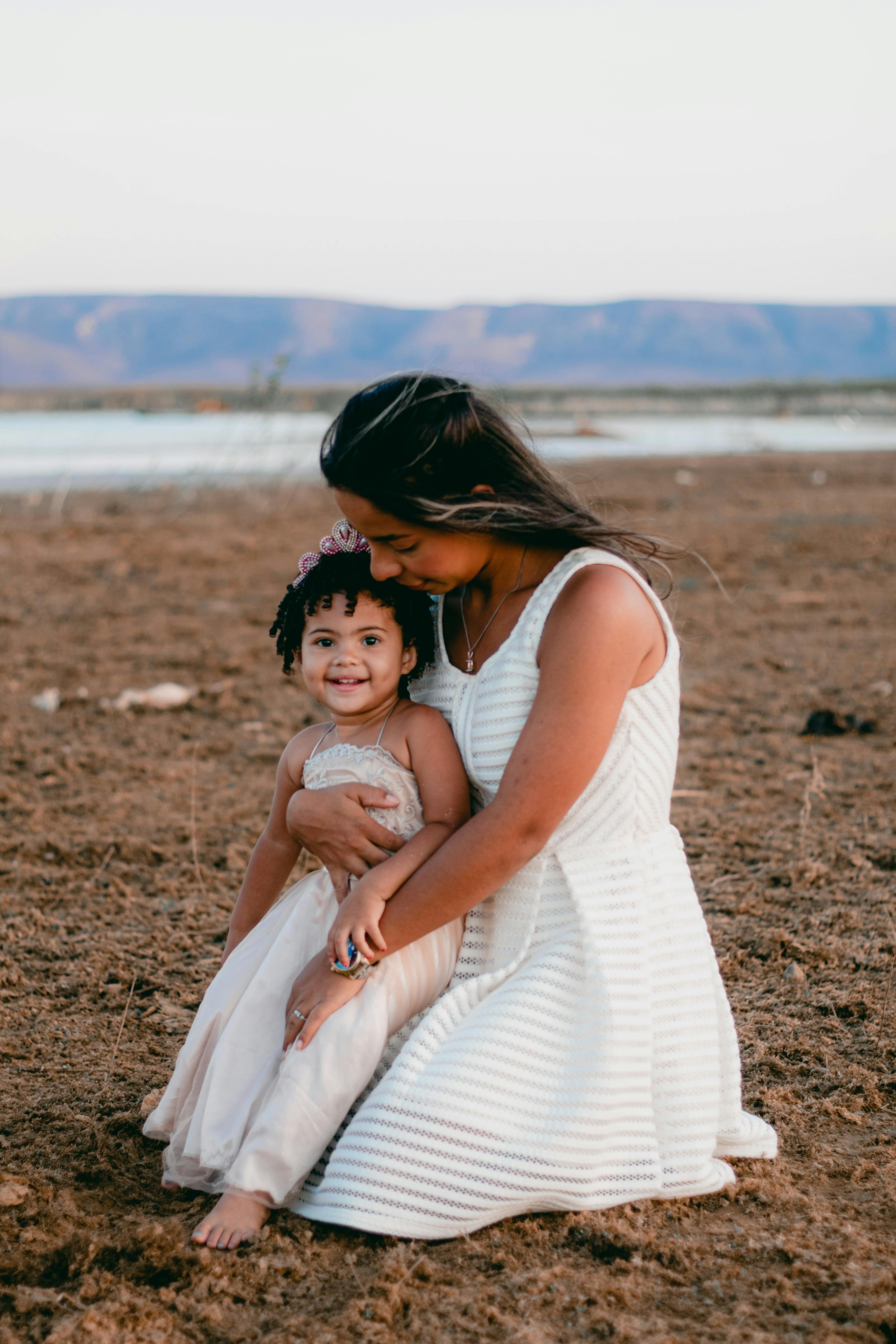 woman with a baby girl wearing dresses sitting on a brown soil