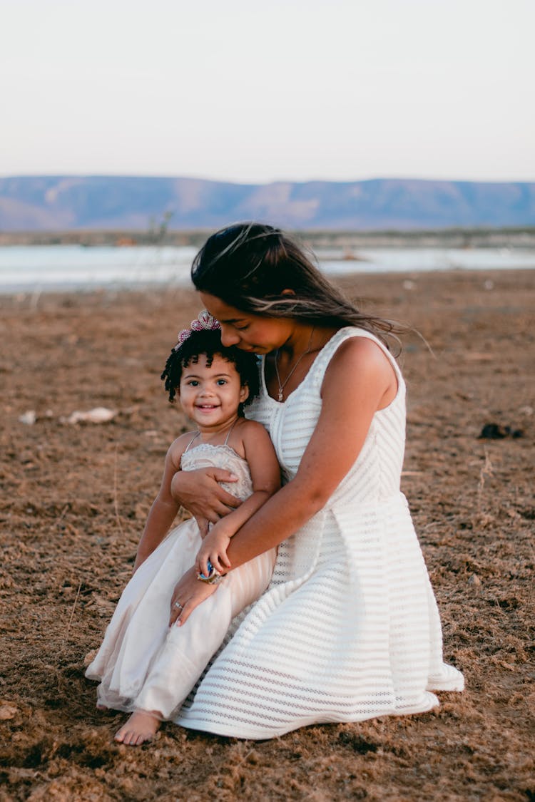 Woman With A Baby Girl Wearing Dresses Sitting On A Brown Soil