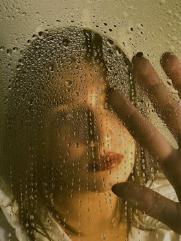 A woman seen through a glass with water droplets, evoking mystery and depth.