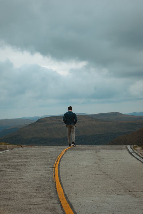 Free A lone person walks along a deserted mountain road under an overcast sky. Stock Photo