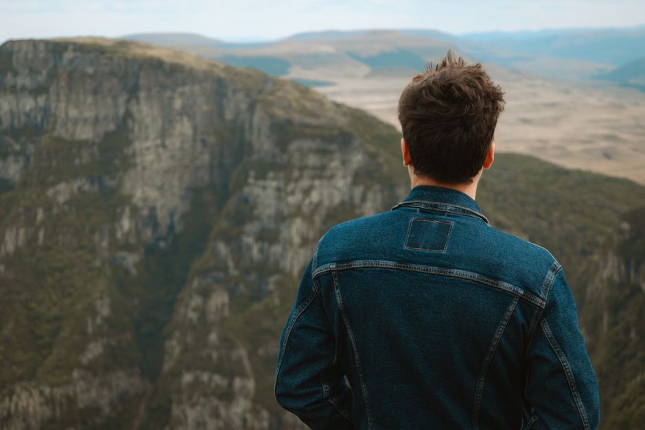 Man in a denim jacket overlooking breathtaking mountain landscape. Adventure and tranquility.