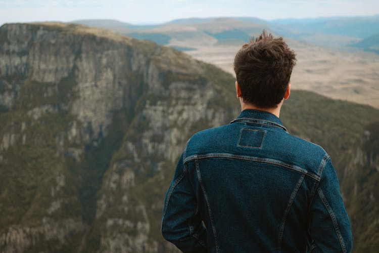 Man In Jean Jacket Standing On Top Of Hill