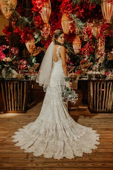 A beautiful bride poses in a lace wedding dress amidst vibrant flowers and warm lighting.
