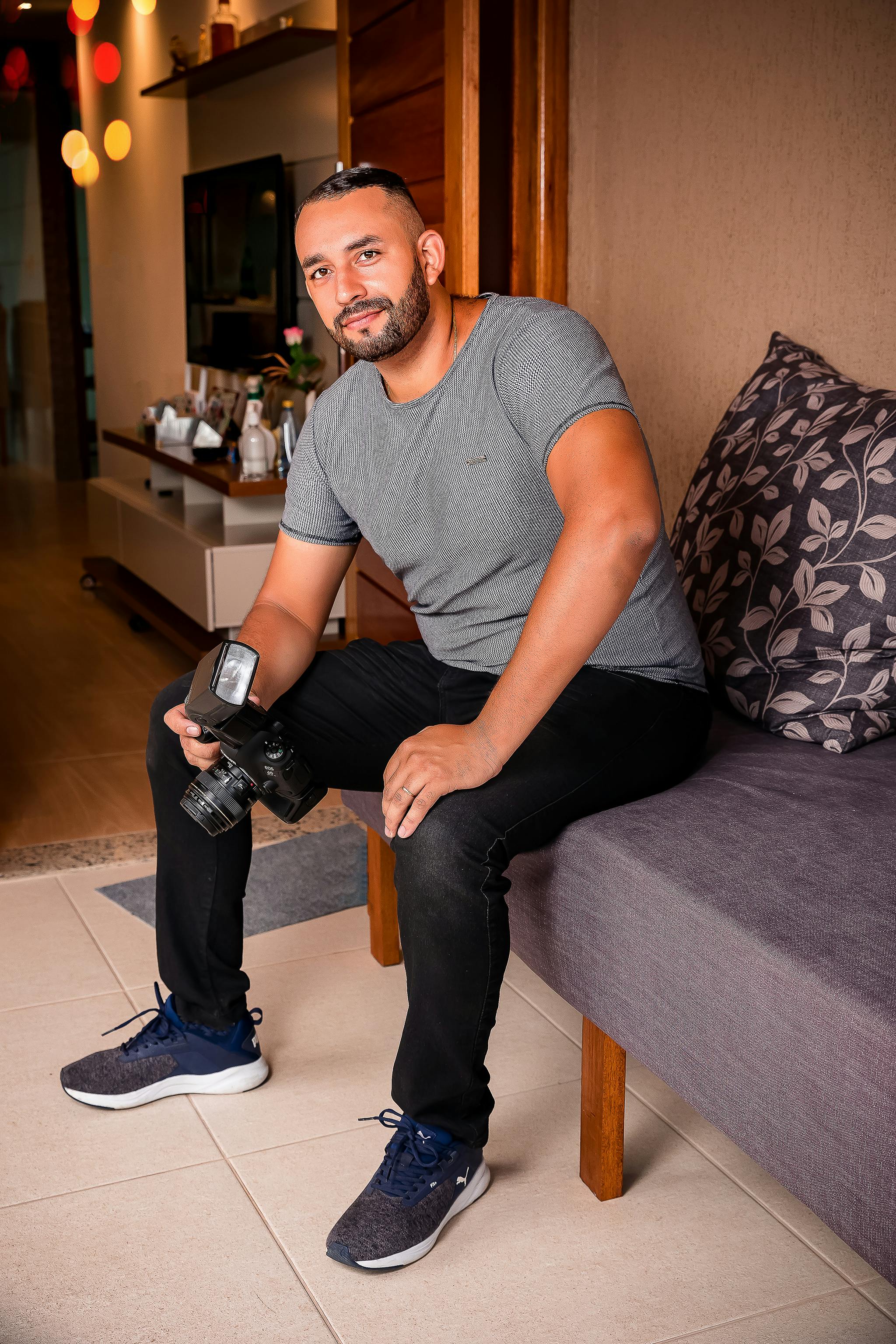 Casual portrait of a man seated on a sofa holding a camera in a contemporary living room.