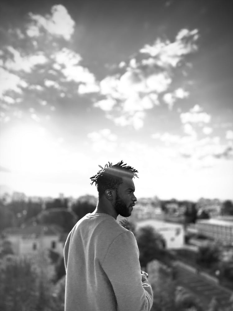 Black And White Photo Of Man Standing On Rooftop Overlooking City