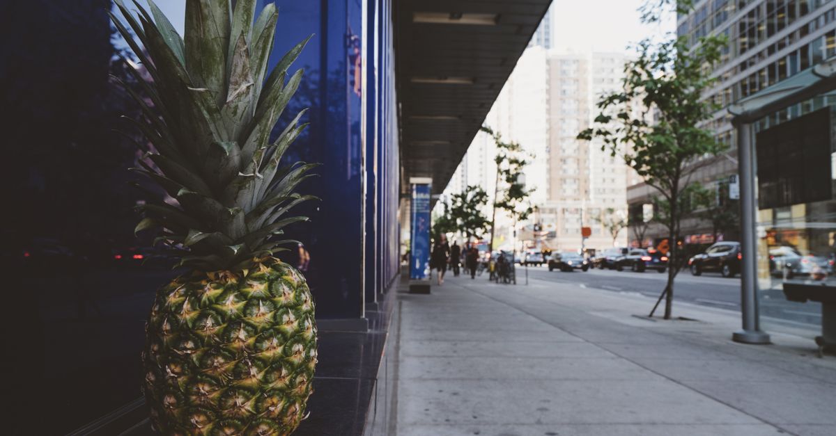 Pineapple placed on sidewalk in bustling urban environment, showcasing modern architecture.