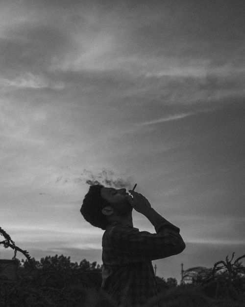 Free Silhouette of a man smoking under a cloudy sky in a monochrome setting Stock Photo