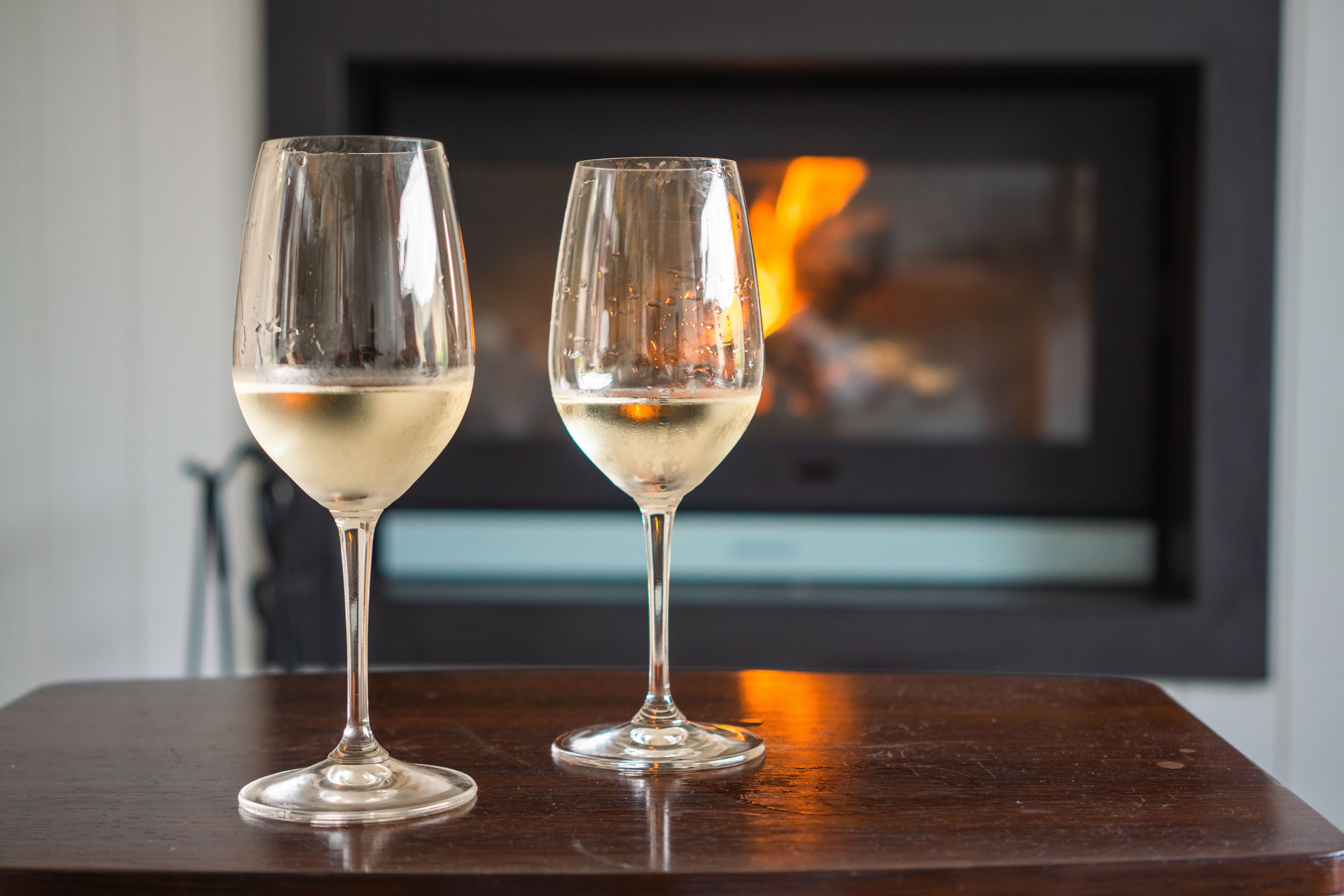 Two glasses of white wine in front of a warm fireplace, evoking a cozy atmosphere.