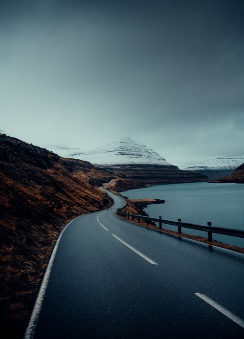 Free A winding road through a serene mountainous landscape with snowcapped peaks under an overcast sky. Stock Photo